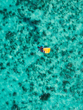 Aerial view of a person wing foiling over the vibrant turquoise waters and coral reef patterns of Mauritius.