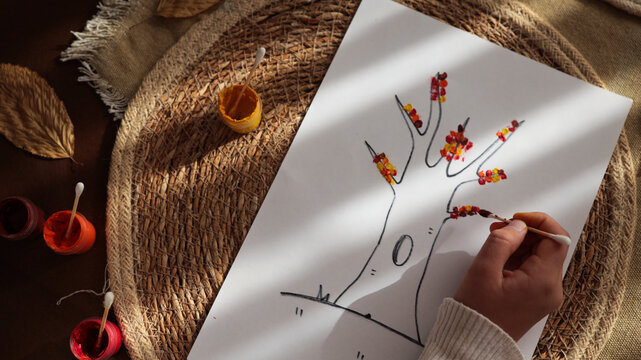 Child's hand creating autumn tree art with cotton swabs and paint