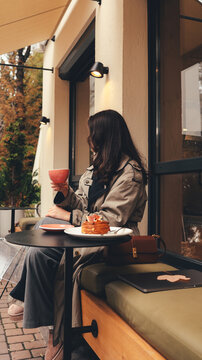 Woman enjoying coffee and pastry at an outdoor cafe during autumn