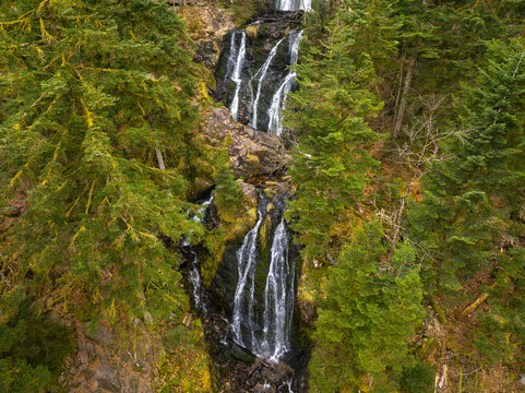 Aerial view of the Grande Cascade de Tendon waterfall cascading down rocky cliffs surrounded by lush evergreen forest in Tendon, Grand Est, France.
