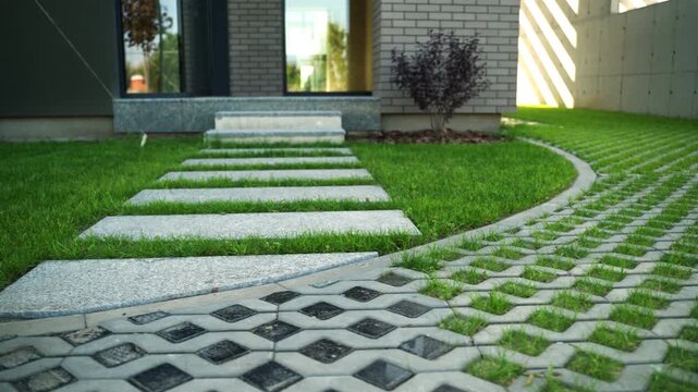 Modern house entrance with green lawn, stone tile pathway, and permeable grass paver driveway showcasing sustainable urban landscape design and architecture on a sunny day