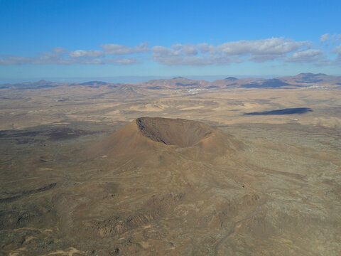 Aerial view of Caldera Los Arrabales volcanic crater set in a rugged arid landscape with volcanic rock formations under a clear blue sky in Las Palmas, Canary Islands, Spain.