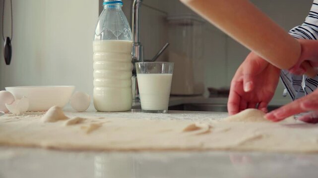 Mother and daughter baking together, rolling out dough with a rolling pin in the kitchen for a homemade pastry