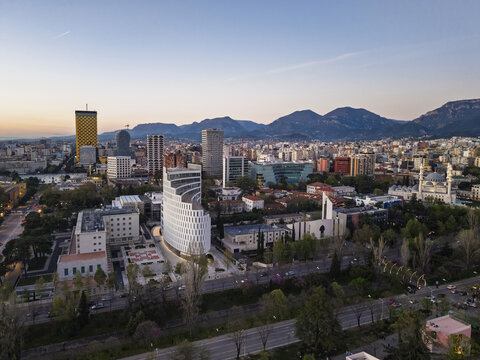 Aerial view of the city of Tirana at sunset, featuring modern architecture, the Et'hem Bey Mosque, and surrounding mountains under a clear sky Tirana, Tirana County, Albania.