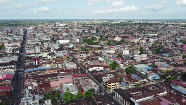 Aerial view of the dense urban landscape of Iquitos, featuring a grid of streets, numerous rooftops, and lush greenery under a cloudy sky in the Amazon rainforest region, Iquitos, Loreto, Peru.