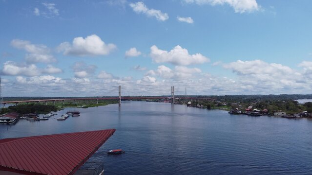 Aerial view of the Nanay Bridge spanning the Nanay River, surrounded by lush Amazon rainforest under a bright blue sky with clouds in Iquitos, Loreto, Peru.