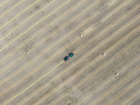 Aerial view of a tractor working in a harvested field with straw bales arranged in rows in Hombourg, Grand Est, France.