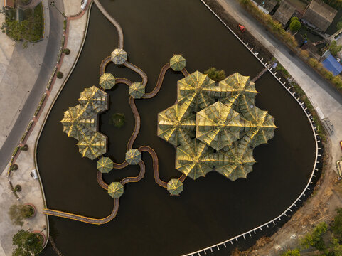 Aerial view of the Pavilion of the Enlightened with its intricate golden roofs surrounded by water and connected by winding walkways in Phraeksa, Samut Prakan, Thailand.