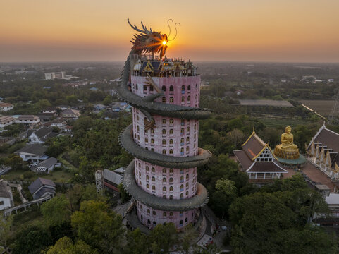 Aerial view of Wat Sam Phran, the iconic pink dragon temple, surrounded by lush greenery and a golden Buddha statue during golden hour in Tambon Sam Phran, Chang Wat Nakhon Path, Thailand.
