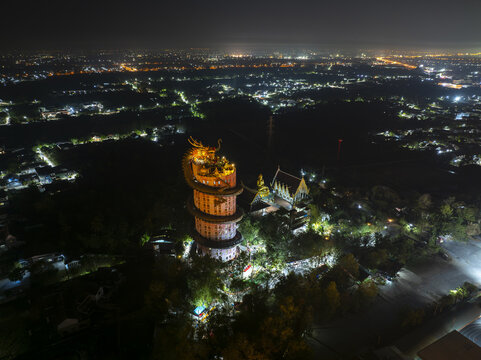 Aerial view of the illuminated Wat Sam Phran dragon temple at night, with its giant dragon sculpture coiled around the pink tower, in Tambon Sam Phran, Nakhon Pathom, Thailand.