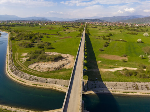 Aerial view of Tsar's Bridge spanning the Zeta River, surrounded by lush green fields and meadows under a clear blue sky in Niksic, Opstina Niksic, Montenegro.