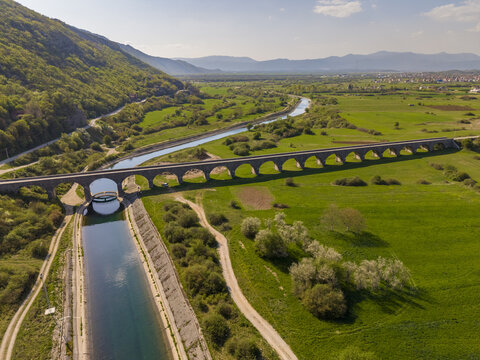 Aerial view of Tsar's Bridge spanning over the Zeta River, surrounded by lush green fields and rolling hills in Niksic, Opstina Niksic, Montenegro.