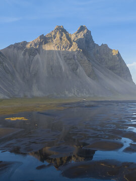 Aerial view of the dramatic jagged peaks of Vestrahorn mountain reflecting in the tidal flats under a clear blue sky in Hofn, Sveitarfelagid Hornaf, Iceland.