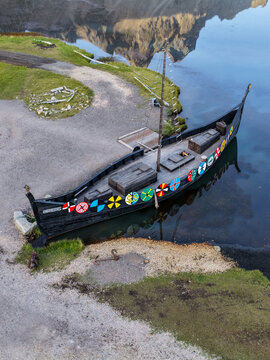 Aerial view of a traditional wooden Viking ship with colorful shields docked at the shore of a calm pond at the Viking Village film set in Hofn, Sveitarfelagid Hornaf, Iceland.