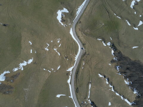 Aerial view of the winding road on Monte Nerone with patches of snow on the grassy slopes in Apecchio, Marche, Italy.