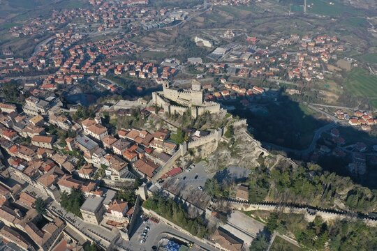 Aerial view of the historic Guaita Tower fortress on Mount Titano, surrounded by stone walls, terracotta rooftops, and the urban landscape of San Marino, San Marino, San Marino.