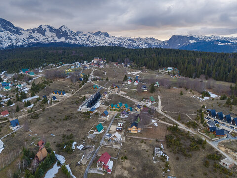 Aerial view of Durmitor National Park featuring alpine chalets scattered across the landscape with snow-capped mountain peaks and pine forests in Zabljak, Zabljak Municipality, Montenegro.