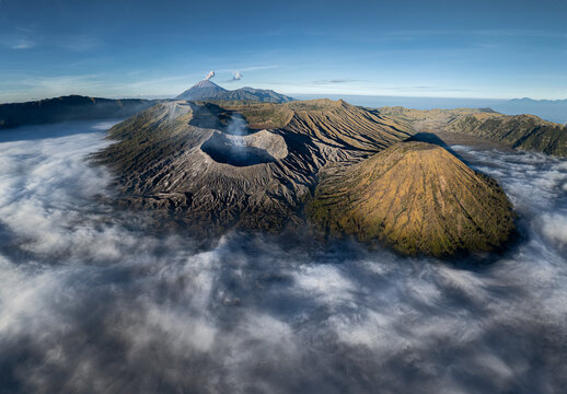 Aerial view of Mount Bromo with its volcanic crater rising above a sea of clouds, surrounded by rugged terrain and Mount Semeru in Kecamatan Sukapura, Jawa Timur, Indonesia.