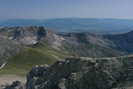 Aerial view of Monte Corvo featuring rugged mountain peaks, rocky slopes, patches of snow, and lush green valleys in the Gran Sasso massif, L'Aquila, Abruzzo, Italy.