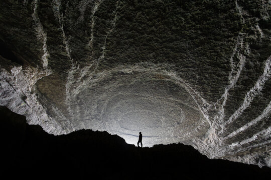 Aerial view of a person standing inside the massive Zhijin Cave with textured rock formations and dramatic lighting in Bijie, Guizhou, China.