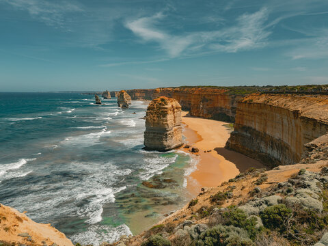 View of the Twelve Apostles limestone stacks along the Great Ocean Road with sandy beach, crashing waves, and rugged cliffs under a clear blue sky in Lorne, Victoria, Australia.
