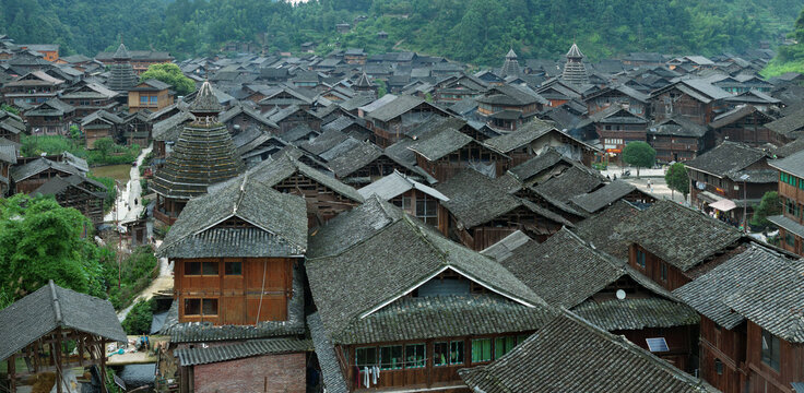 Aerial view of the traditional wooden houses with grey tiled roofs and distinctive drum towers in the Dong ethnic village of Huanggang Village, Guizhou, China.