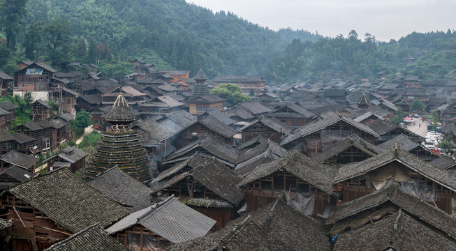 Aerial view of the traditional wooden houses and distinctive drum tower of Huanggang Village nestled among lush green hills in Huanggang Village, Guizhou, China.