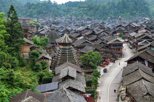 Aerial view of traditional wooden houses and distinctive drum towers nestled among lush green hills in Huanggang Village, Guizhou, China.