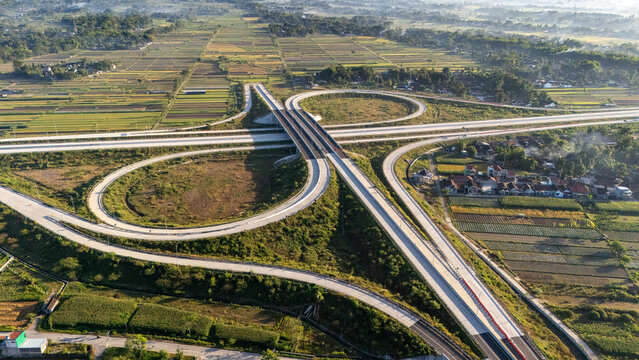 Aerial view of a modern highway interchange surrounded by lush agricultural fields and rural houses in Indonesia.