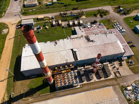 Aerial view of Tinian power station featuring industrial buildings with metal roofs, red and white smokestacks, and cooling units in San Jose, Tinian, Northern Mariana Islands.