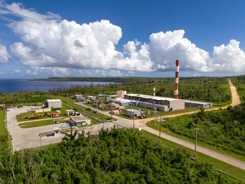 Aerial view of Tinian power station with red and white smokestacks, surrounded by lush vegetation and coastal scenery in San Jose, Tinian, Northern Mariana Islands.