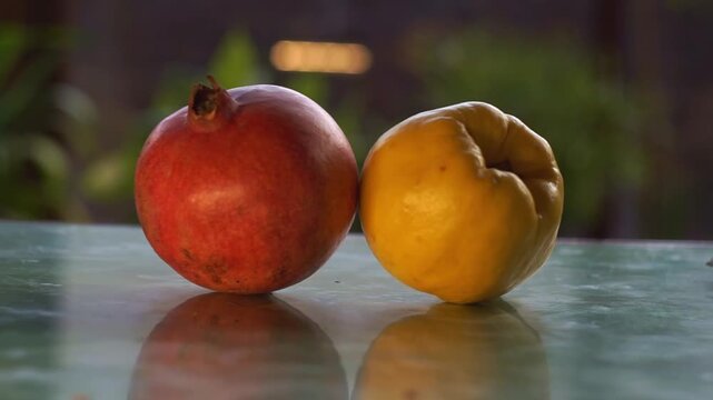 Close up slow motion camera panning of a fresh red pomegranate and a ripe yellow quince fruit on a glossy surface, horizontal video.