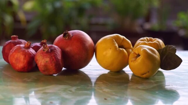 Slow motion camera panning of fresh red pomegranates and ripe yellow quinces in a row on a glossy table, horizontal video.