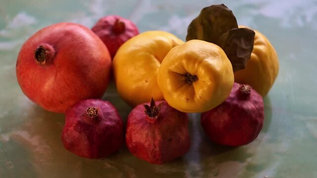 Slow motion camera panning of ripe yellow quinces with green leaves and red pomegranates on a textured surface, horizontal video.
