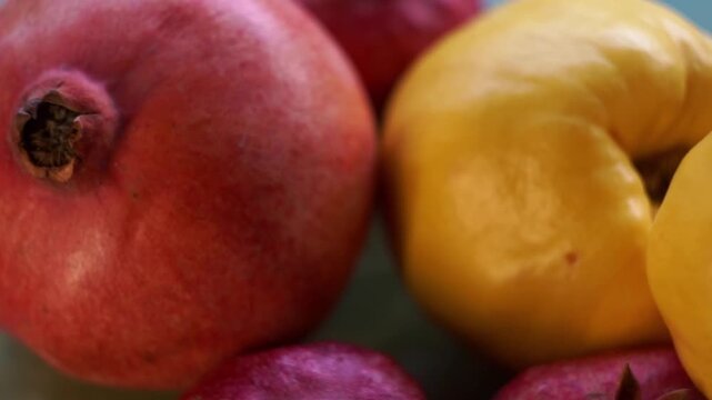Extreme close up slow motion camera panning of ripe yellow quinces and fresh red pomegranates with shallow depth of field, horizontal video.