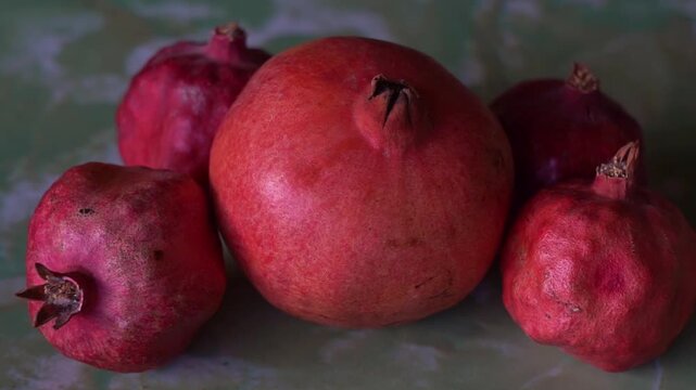Slow motion camera panning of a group of whole red pomegranates on a green textured surface, horizontal video.