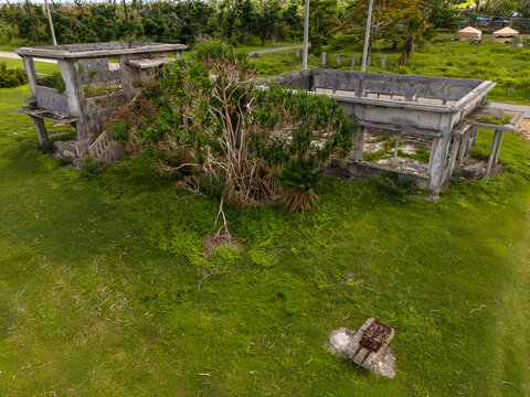 Aerial view of the historic Old Japanese Sugar Company HQ ruins, featuring weathered concrete walls and overgrown vegetation in a grassy field in San Jose, Tinian, Northern Mariana Islands.