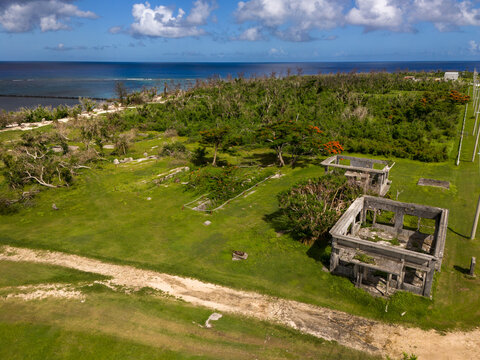 Aerial view of the Old Japanese Sugar Company HQ ruins surrounded by lush greenery and a dirt path near the coastline in San Jose, Tinian, Northern Mariana Islands.