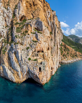 Aerial view from the sea toward the mountain at Porto Flavia, showing the balcony and mining tunnel entrance marked with its historic sign in Sardinia, Italy.