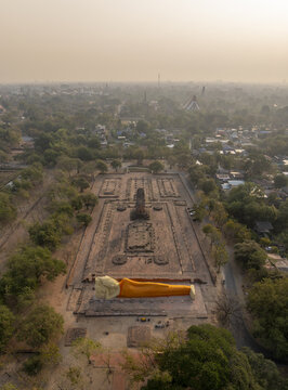 Aerial view of Wat Lokaya Sutha with its large reclining Buddha statue draped in an orange robe amidst ancient brick ruins in Phra Nakhon Si Ayutthaya, Thailand.