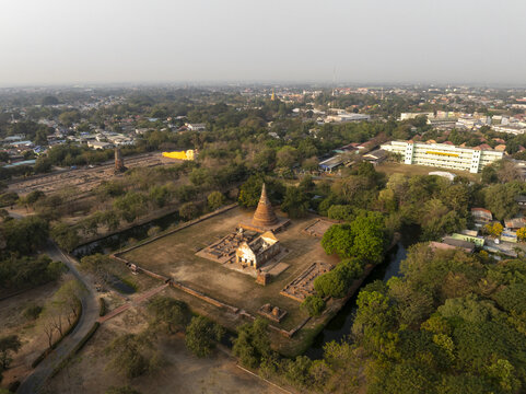 Aerial view of the historic Wat Maheyong temple ruins surrounded by lush trees, a moat, and modern urban buildings in Thailand.