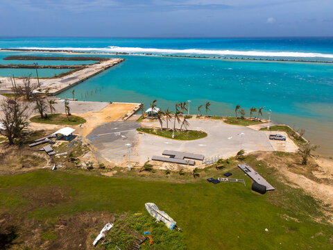 San Jose, Tinian, Northern Mariana Islands - 07 July 2026: Aerial view of Tinian Marina showing significant storm surge damage and debris scattered across the parking area following a typhoon.