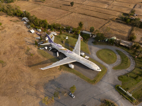 Aerial view of a retired airplane converted into a cafe parked in a dry field with surrounding trees and paved pathways in Thailand.
