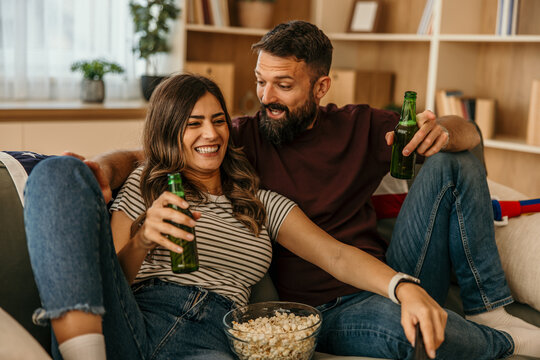 Happy couple relaxing on sofa drinking beer watching tv