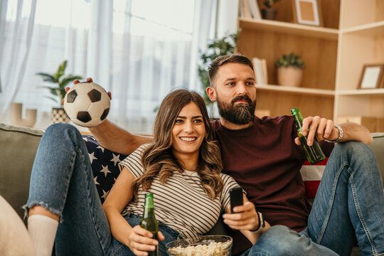 Couple watching soccer game at home enjoying beer and popcorn