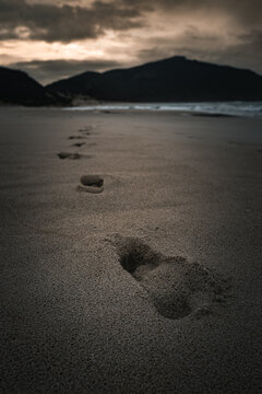View of footprints in the sand leading towards Conspicuous Cliff on a moody day at the beach in Nornalup, Western Australia, Australia.