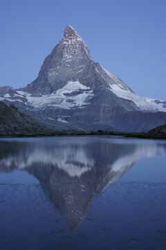 View of the Matterhorn reflecting in a calm alpine lake with snow-capped peaks under a clear blue sky in Switzerland.
