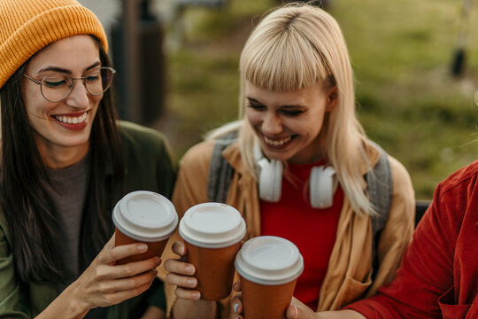 Friends toasting coffee cups outdoors and laughing together