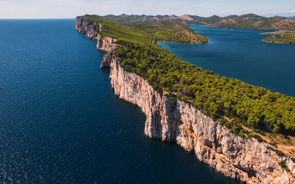 Aerial view of the dramatic limestone cliffs of Telascica Nature Park covered in lush pine forests, overlooking the deep blue Adriatic Sea in Sali, Zadar County, Croatia.