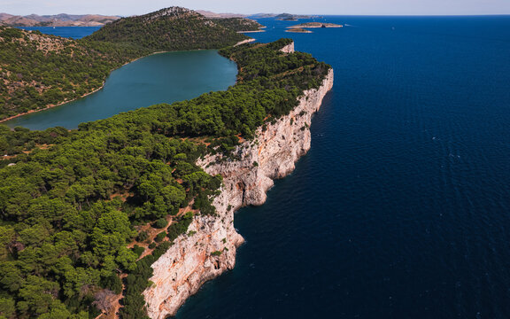 Aerial view of Telascica Nature Park featuring dramatic limestone cliffs, deep blue Adriatic Sea, and a salt lake nestled among lush pine forests in Sali, Zadar County, Croatia.
